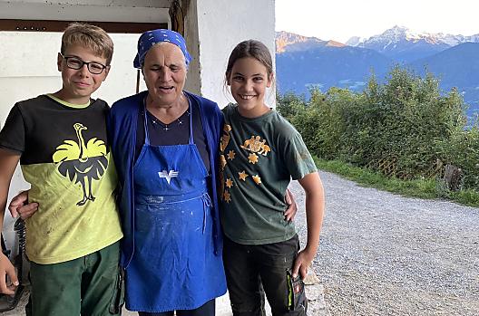 De oude boerin Cilli met kinderen van gasten na het melken in de stal. De familie Stocker vindt het altijd fijn om het leven op de boerderij met hun gasten te delen.
