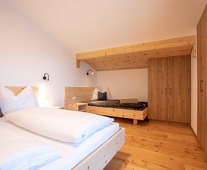  Schlafzimmer mit Doppelbett in Zirbenholz und direktem Zugang zum Balkon.